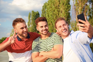 Photo of Happy young men taking selfie outdoors on sunny day