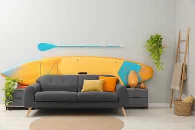 SUP board, paddle and stylish sofa in living room. Interior design