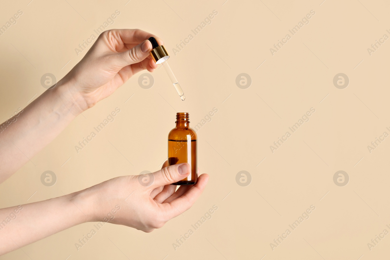 Photo of Woman holding bottle of cosmetic oil on beige background, closeup. Space for text