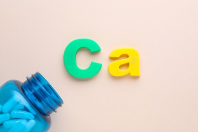 Photo of Open bottle and calcium symbol made of colorful letters on beige background, flat lay