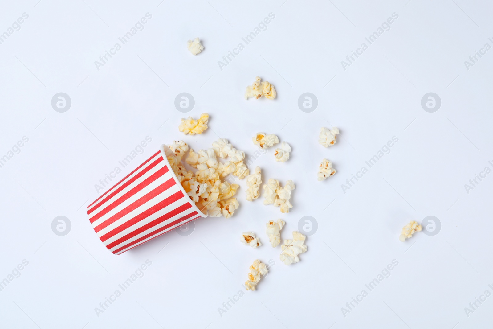 Photo of Overturned paper cup with tasty popcorn on white background, top view