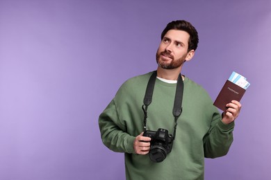 Smiling man with passport, camera and tickets on purple background. Space for text