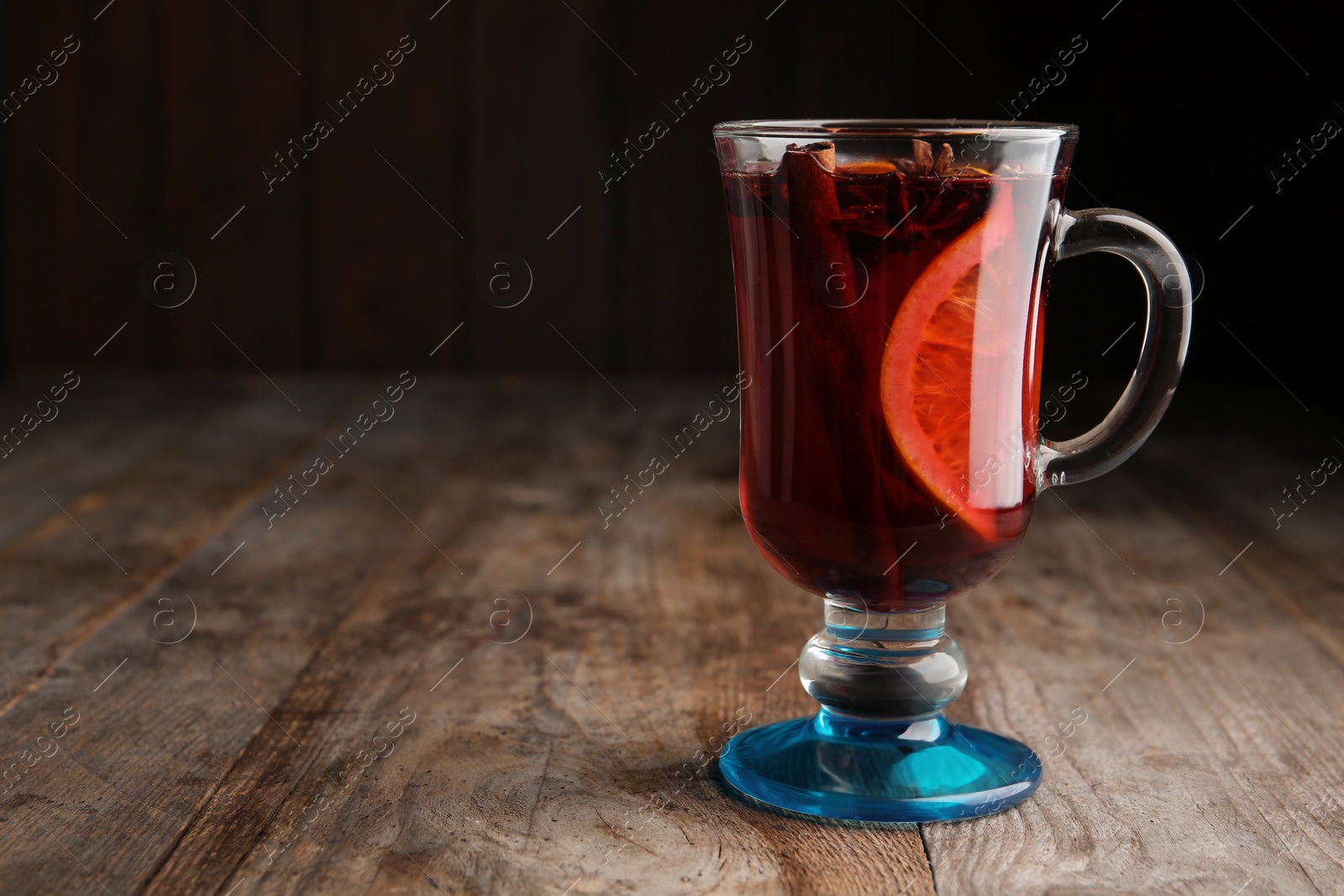 Photo of Glass with red mulled wine on wooden table. Space for text