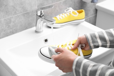 Photo of Woman washing stylish sneakers with brush in sink, closeup