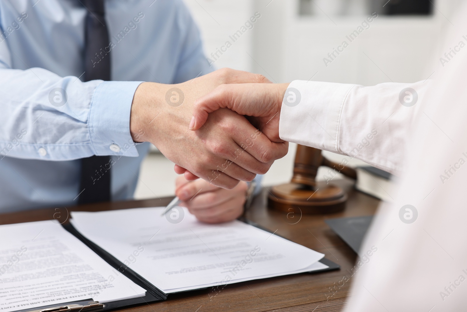 Photo of Lawyers shaking hands at wooden table in office, closeup