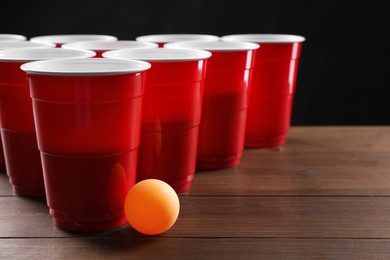 Photo of Plastic cups and ball for beer pong on wooden table against black background