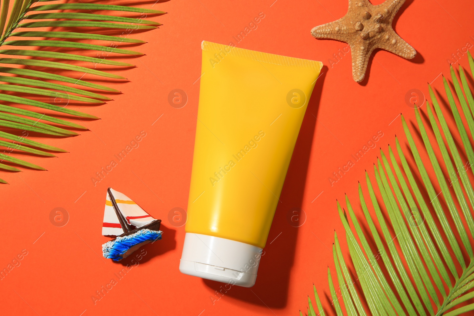 Photo of Sunscreen, starfish, toy sailboat and tropical leaves on coral background, flat lay. Sun protection care