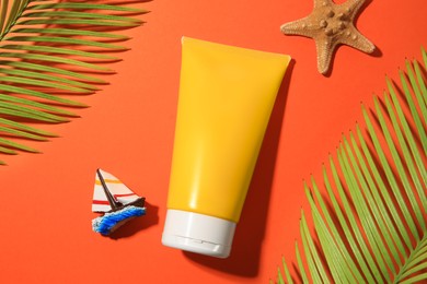 Photo of Sunscreen, starfish, toy sailboat and tropical leaves on coral background, flat lay. Sun protection care