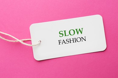 Image of Conscious consumption. Tag with words Slow Fashion on pink background, top view