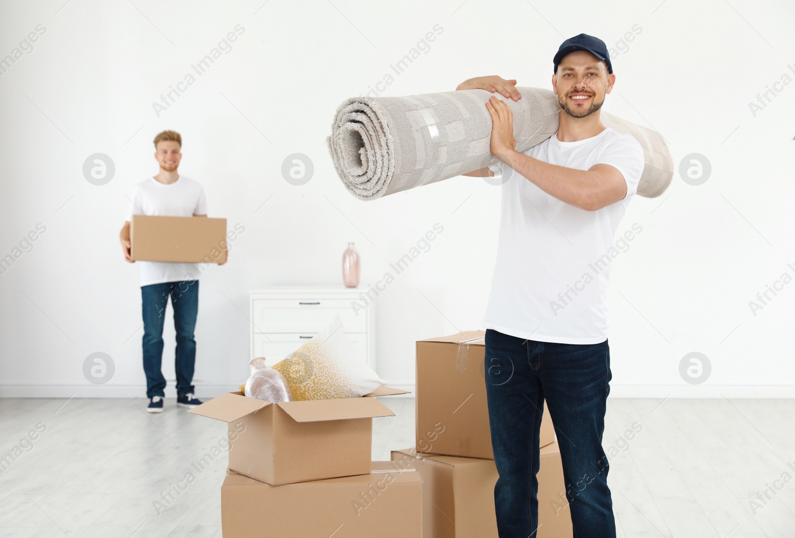 Photo of Moving service employees with cardboard boxes and carpet in room