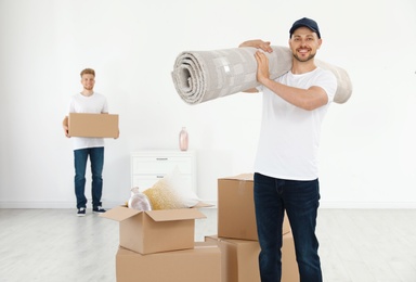 Moving service employees with cardboard boxes and carpet in room