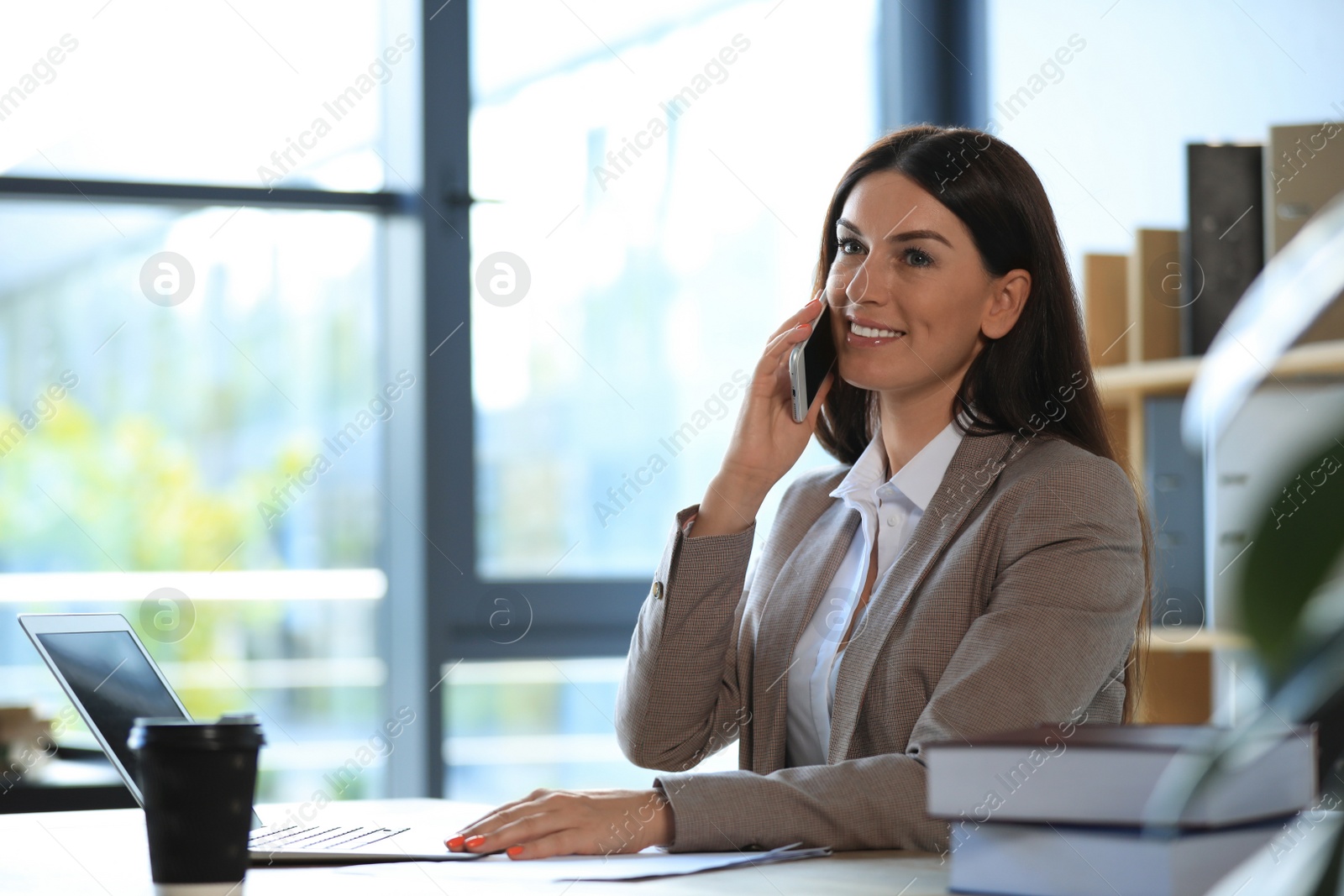 Photo of Female business trainer talking on phone while working with laptop in office