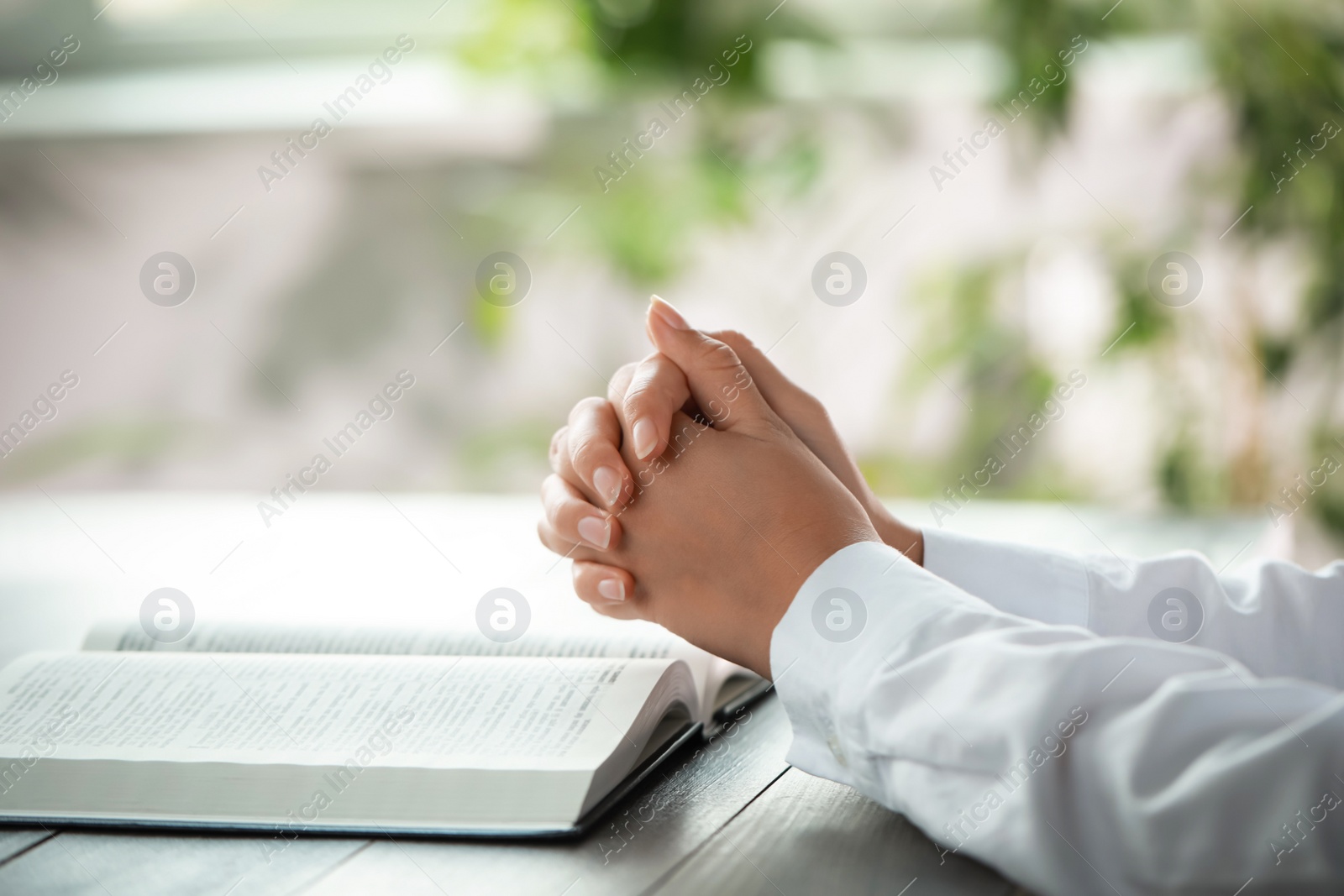 Photo of Woman holding hands clasped while praying at grey wooden table with Bible, closeup