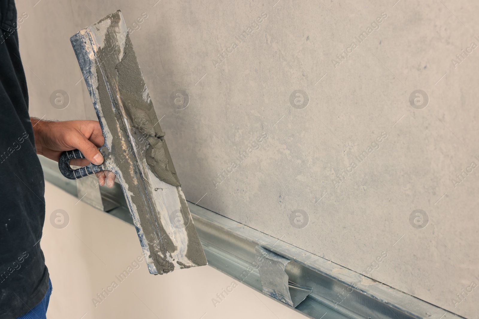 Photo of Worker with spatula near tile on wall indoors, closeup