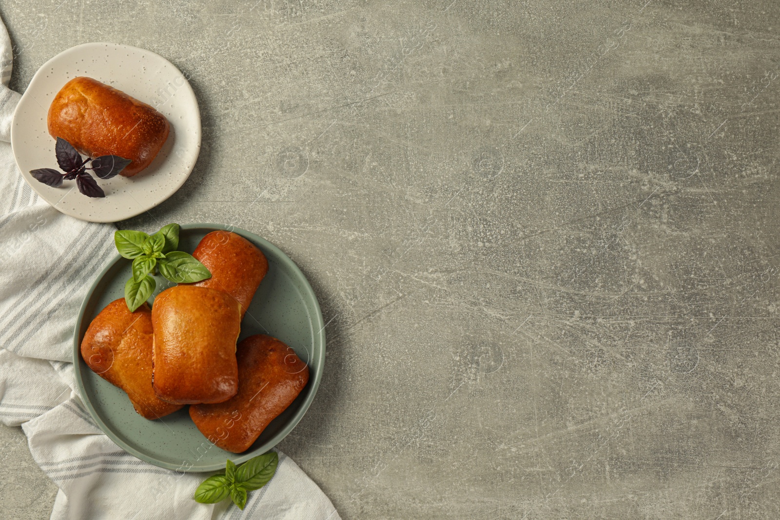 Photo of Delicious baked pirozhki and basil on light grey table, flat lay. Space for text