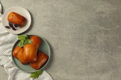 Delicious baked pirozhki and basil on light grey table, flat lay. Space for text