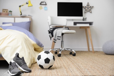 Soccer ball and sneakers near bed in teenager's room interior