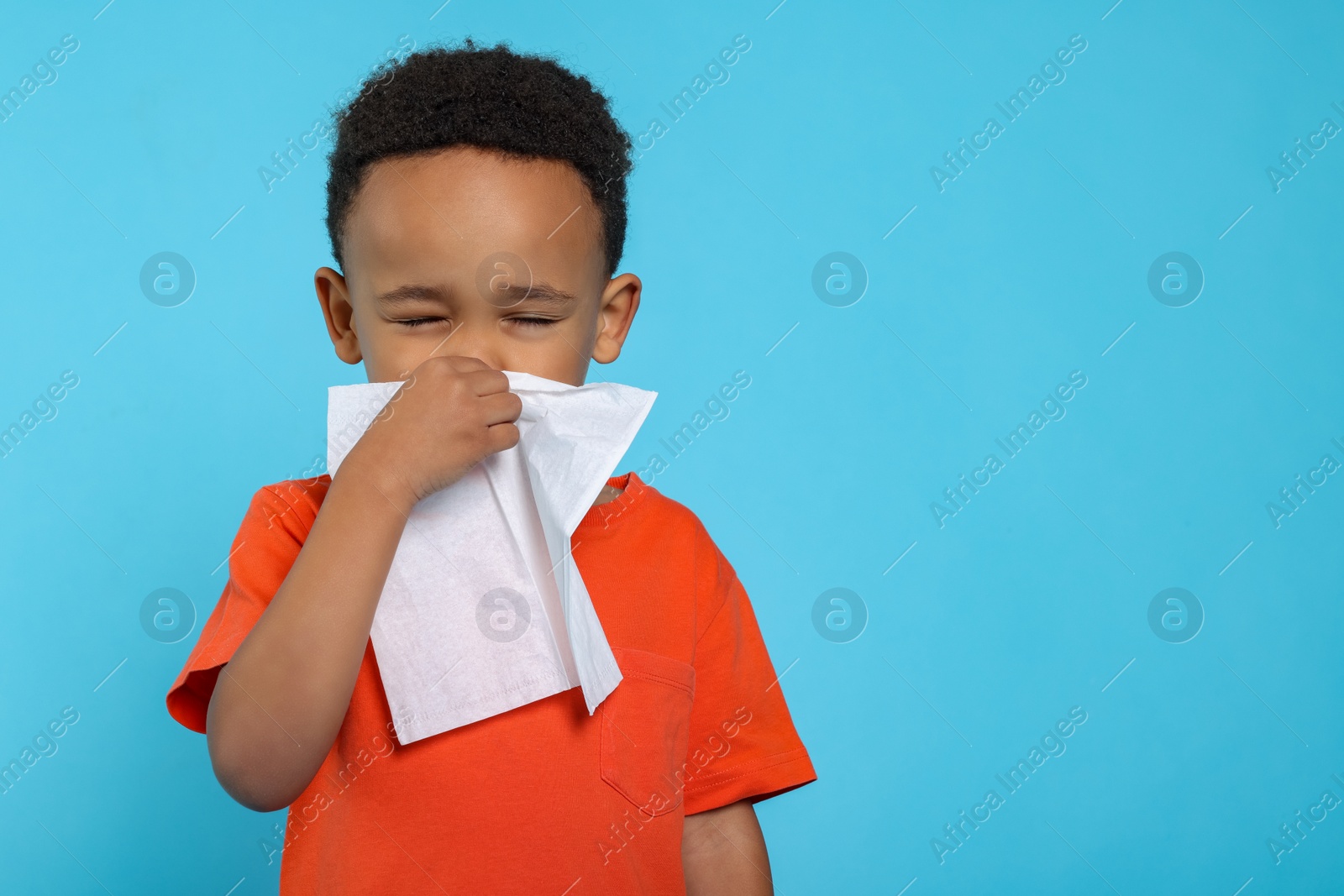 Photo of African-American boy blowing nose in tissue on turquoise background, space for text. Cold symptoms