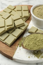 Pieces of tasty matcha chocolate bar and powder on white table, closeup