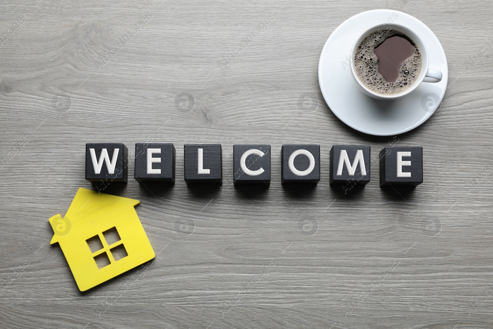 Photo of Black cubes with word Welcome, house model and cup of coffee on wooden table, flat lay