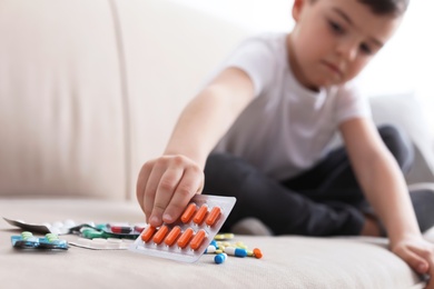 Photo of Little child with different pills on sofa at home. Household danger