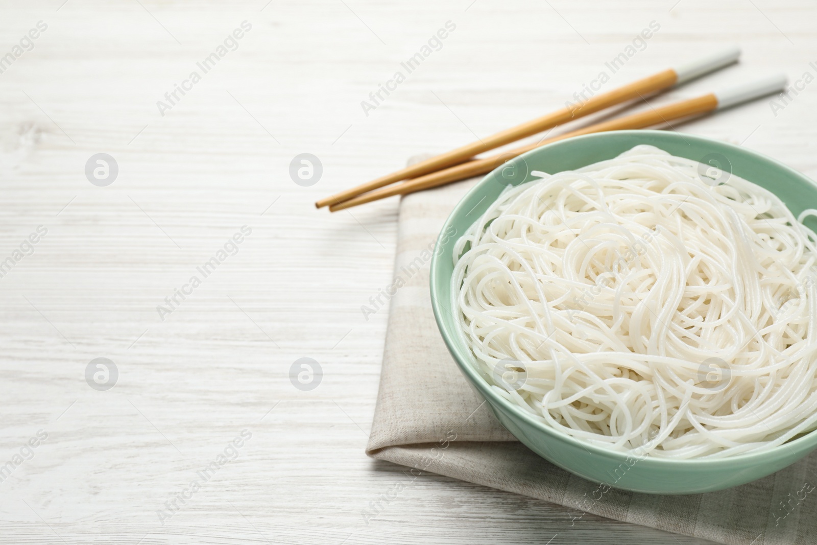 Photo of Bowl with cooked rice noodles and chopsticks on white wooden table. Space for text
