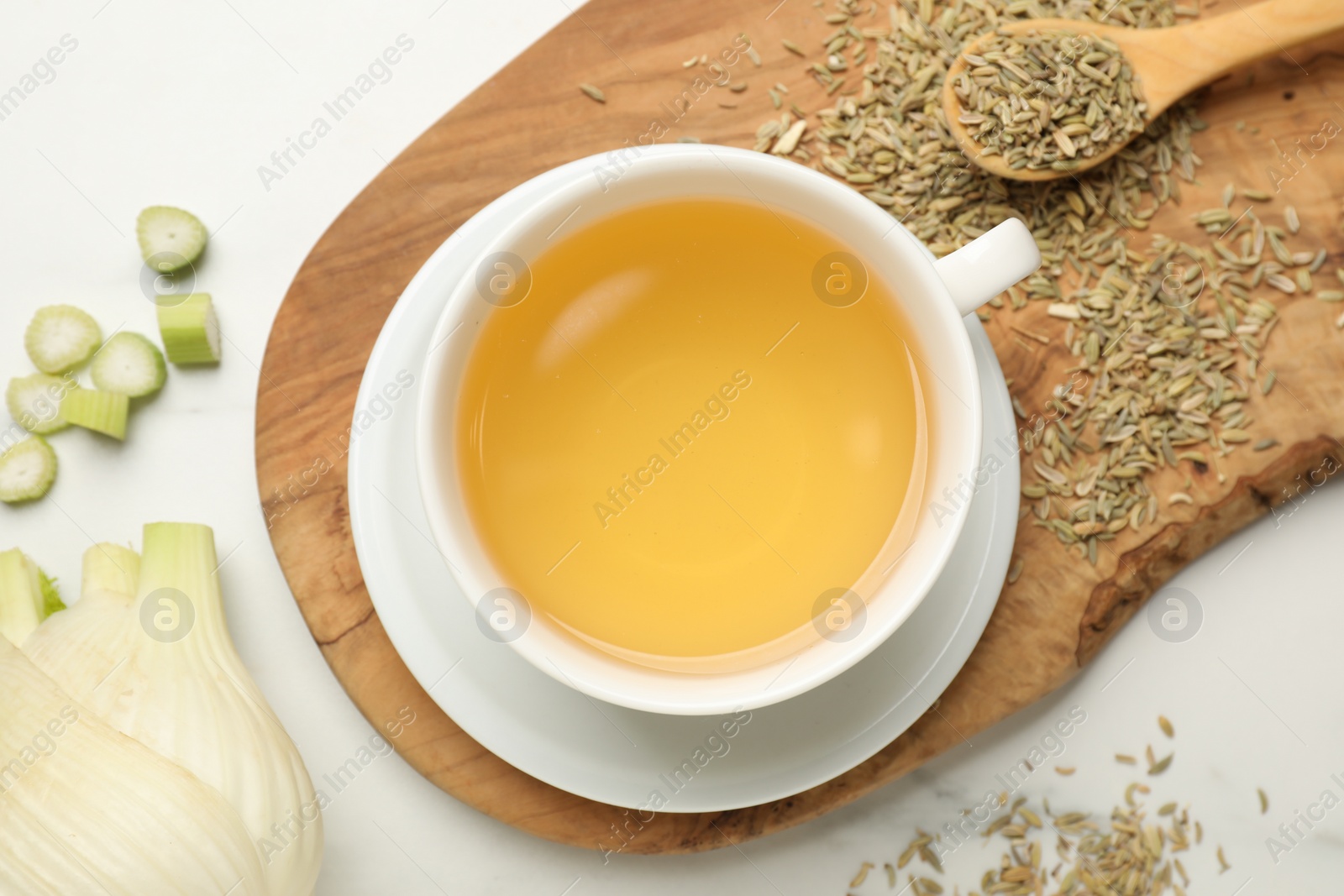 Photo of Fennel tea in cup, seeds and fresh vegetable on white marble table, flat lay