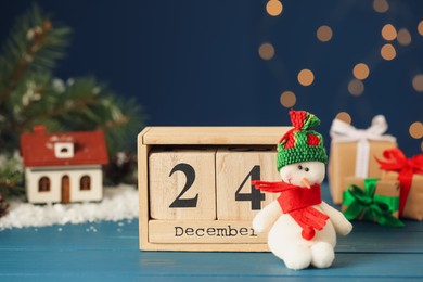 Photo of Christmas Eve - December 24. Block calendar and cute toy snowman on light blue wooden table