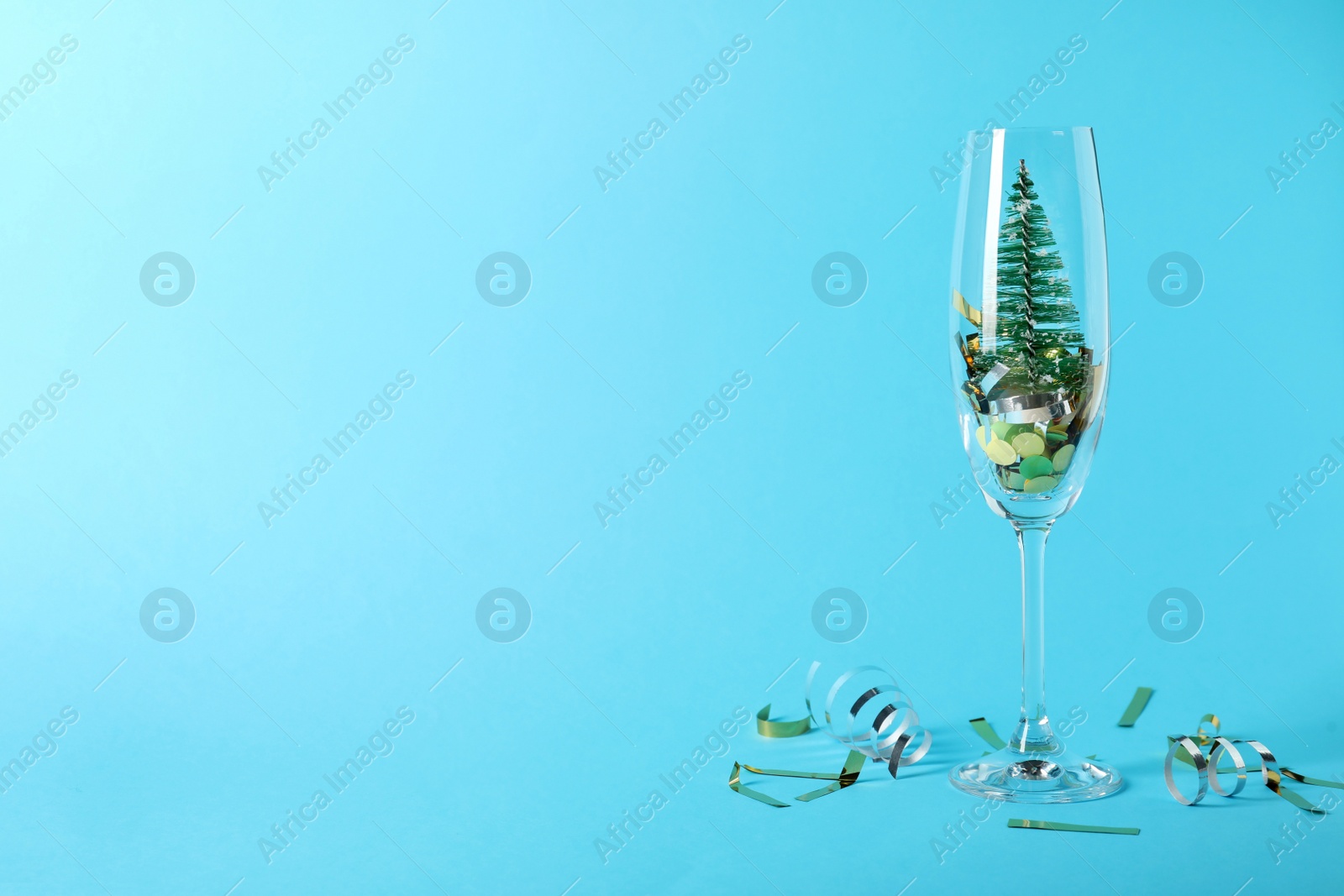 Photo of Glass with decorative tree and confetti on light blue background. Space for text