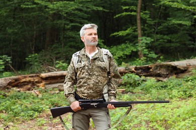 Man with hunting rifle and backpack wearing camouflage in forest