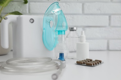 Photo of Modern nebulizer with face mask and medicines on white table near brick wall. Equipment for inhalation