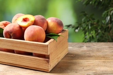 Photo of Cut and whole fresh ripe peaches in crate on wooden table against blurred background, closeup. Space for text