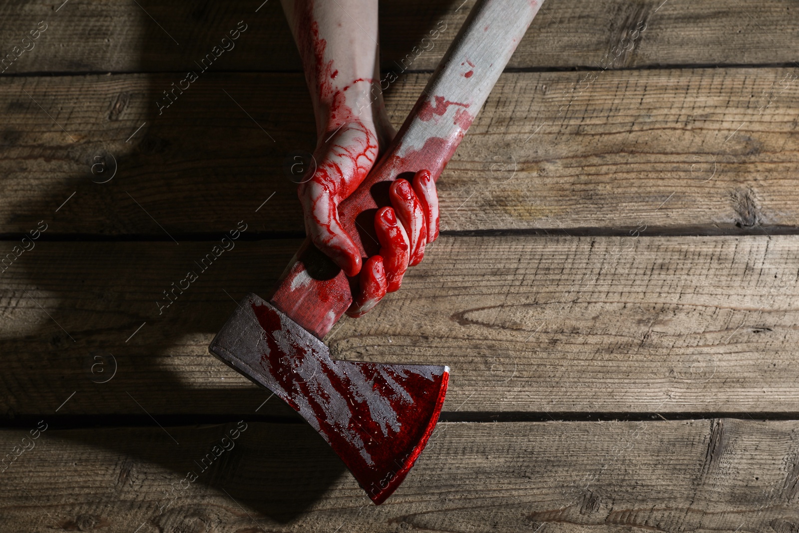 Photo of Man holding bloody axe on wooden surface, top view