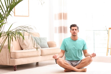 Photo of Man meditating on floor in living room, space for text. Zen concept