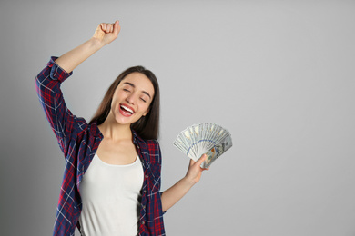 Emotional young woman with money on light grey background. Space for text