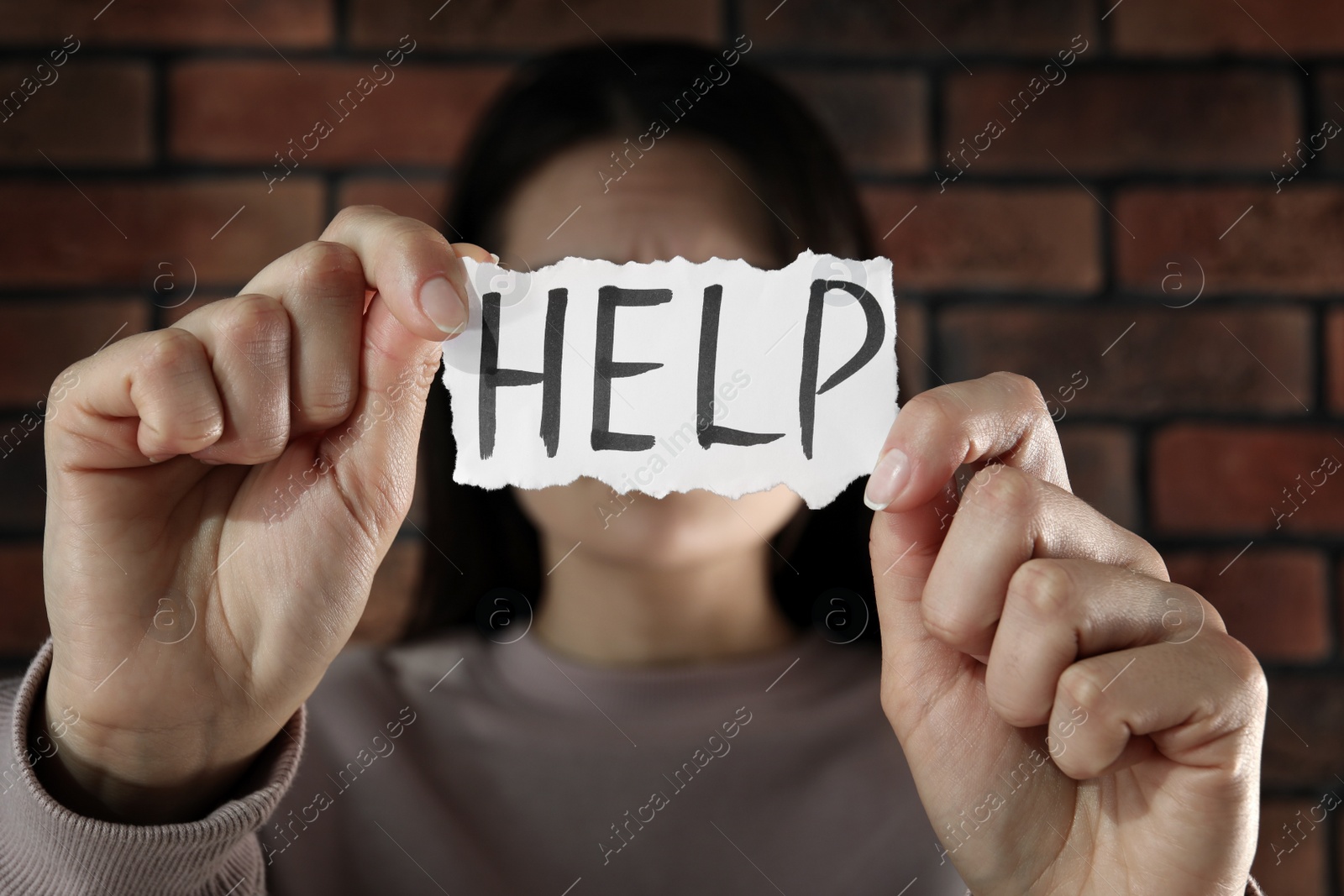 Photo of Domestic violence concept. Woman holding paper with written word Help near brick wall, focus on hands