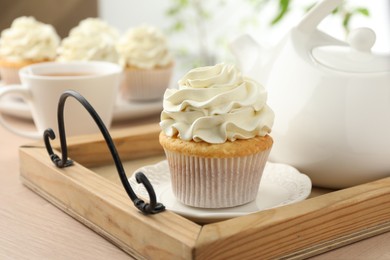 Photo of Tasty cupcake with vanilla cream and teapot on light wooden table, closeup