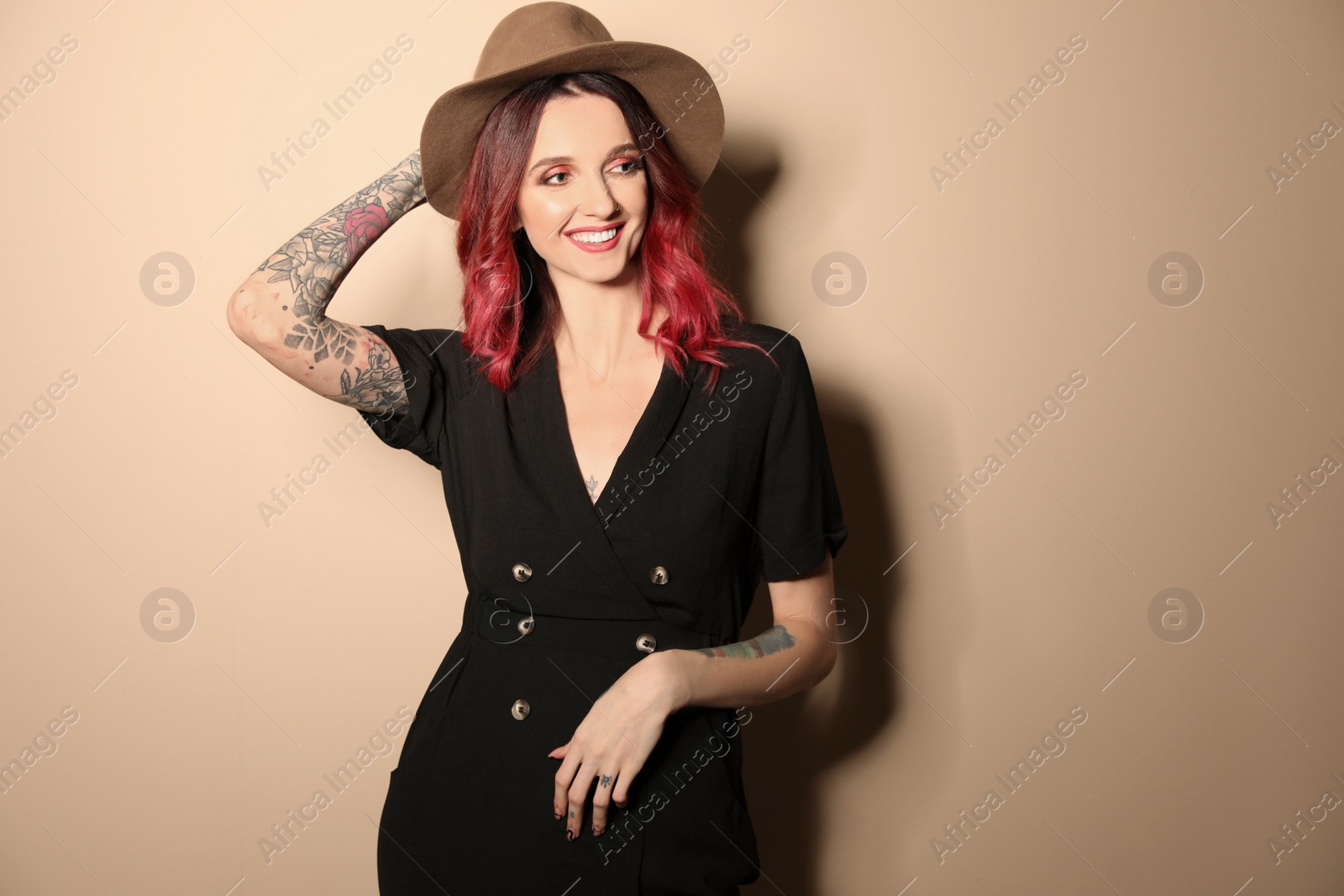 Photo of Beautiful woman with tattoos on arms against beige background