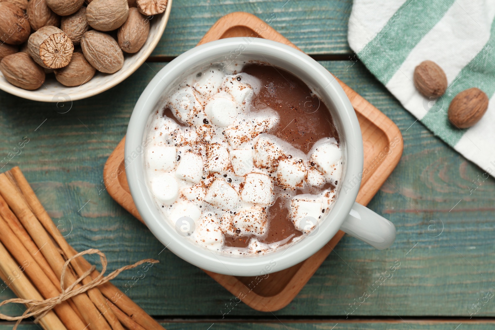 Photo of Hot drink with marshmallows and nutmeg powder on blue wooden table, flat lay