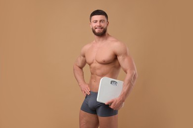 Photo of Smiling athletic man holding scales on brown background. Weight loss concept