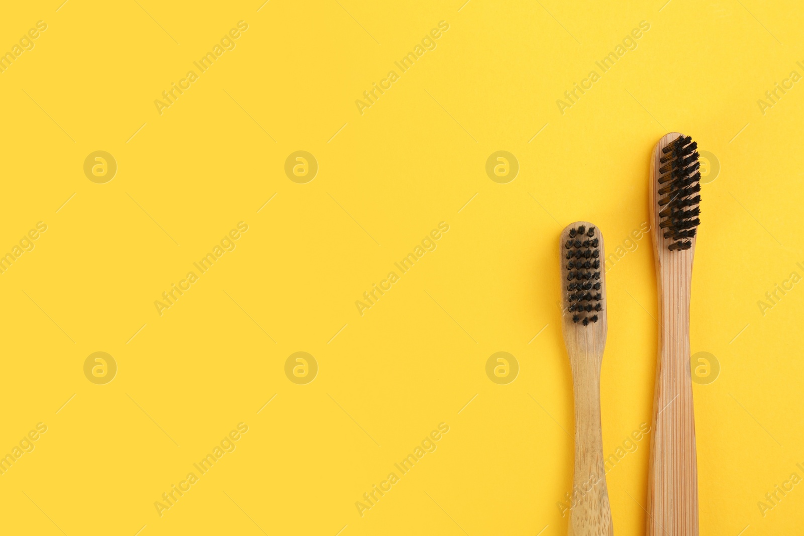 Photo of Toothbrushes made of bamboo on yellow background, flat lay. Space for text