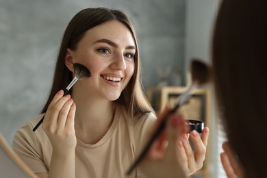 Smiling woman with freckles applying makeup near mirror indoors