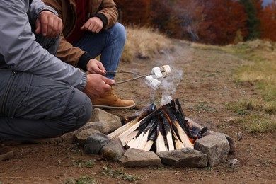 Photo of Men roasting marshmallows over campfire outdoors, closeup. Camping season