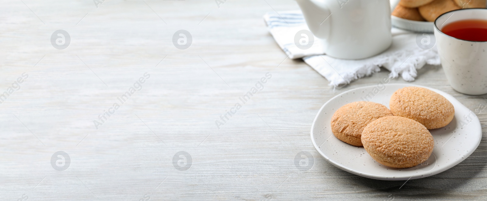 Photo of Delicious sugar cookies and cup of tea on white wooden table, space for text