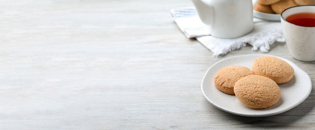 Photo of Delicious sugar cookies and cup of tea on white wooden table, space for text