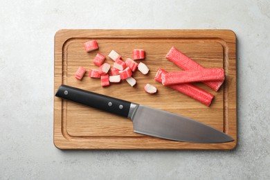 Board with cut crab sticks and knife on light table, top view