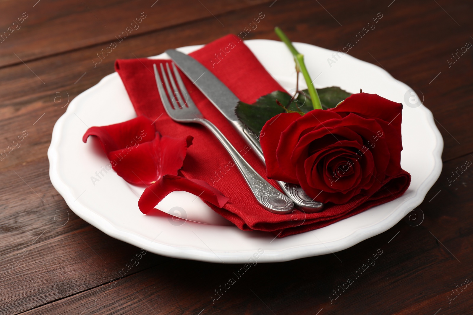 Photo of Romantic place setting with red rose on wooden table. St. Valentine's day dinner