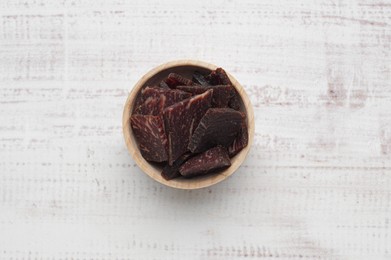 Delicious beef jerky in bowl on wooden table, top view