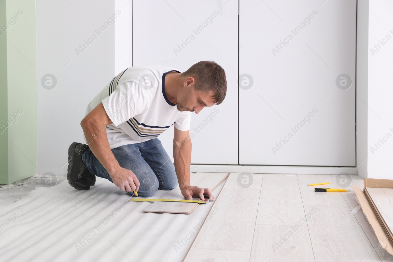 Photo of Man using pencil during installation of new laminate flooring in room