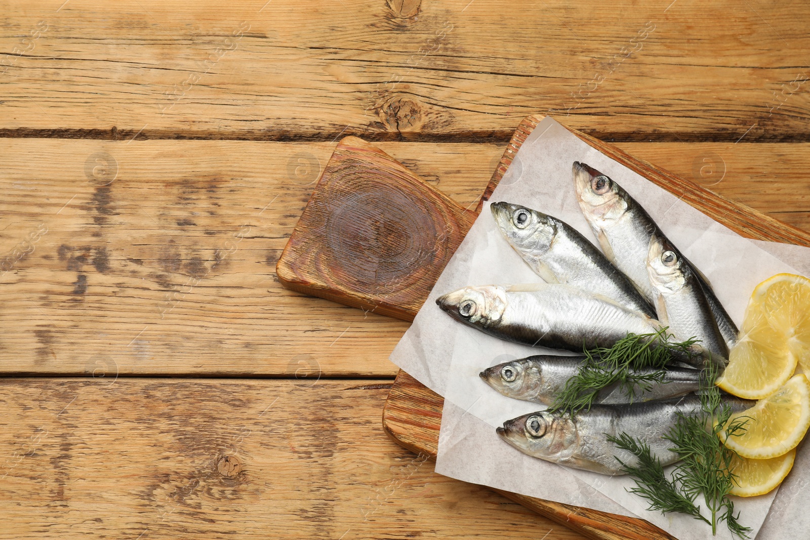 Photo of Fresh raw sprats, lemon and dill on wooden table, top view. Space for text